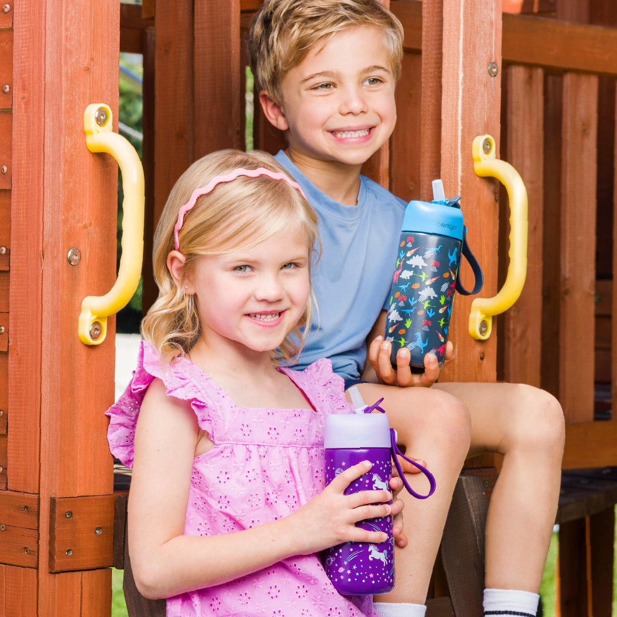 Two children holding colorful water bottles on a playground.