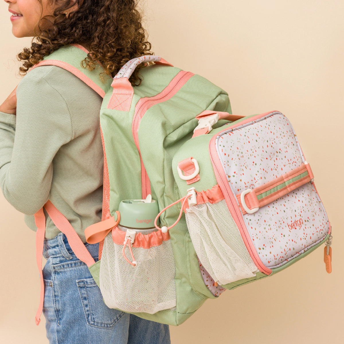 Person wearing a green and pink backpack with multiple compartments on a beige background