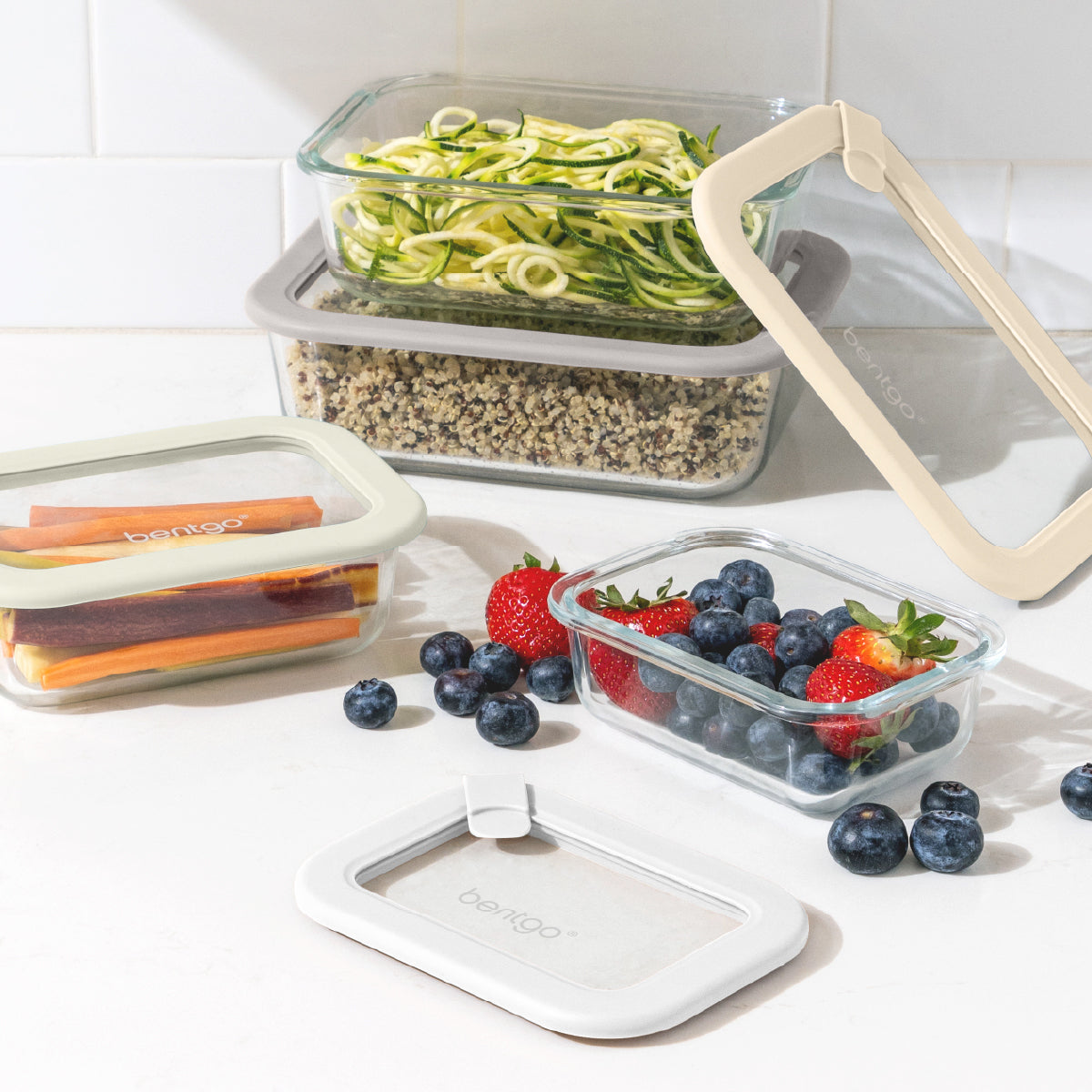 Set of food storage containers with lids containing vegetables, berries, and fruits on a white surface.