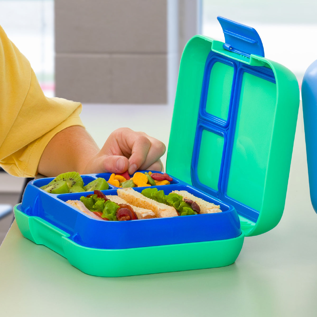 Green and blue bento box with compartments filled with food on a table.