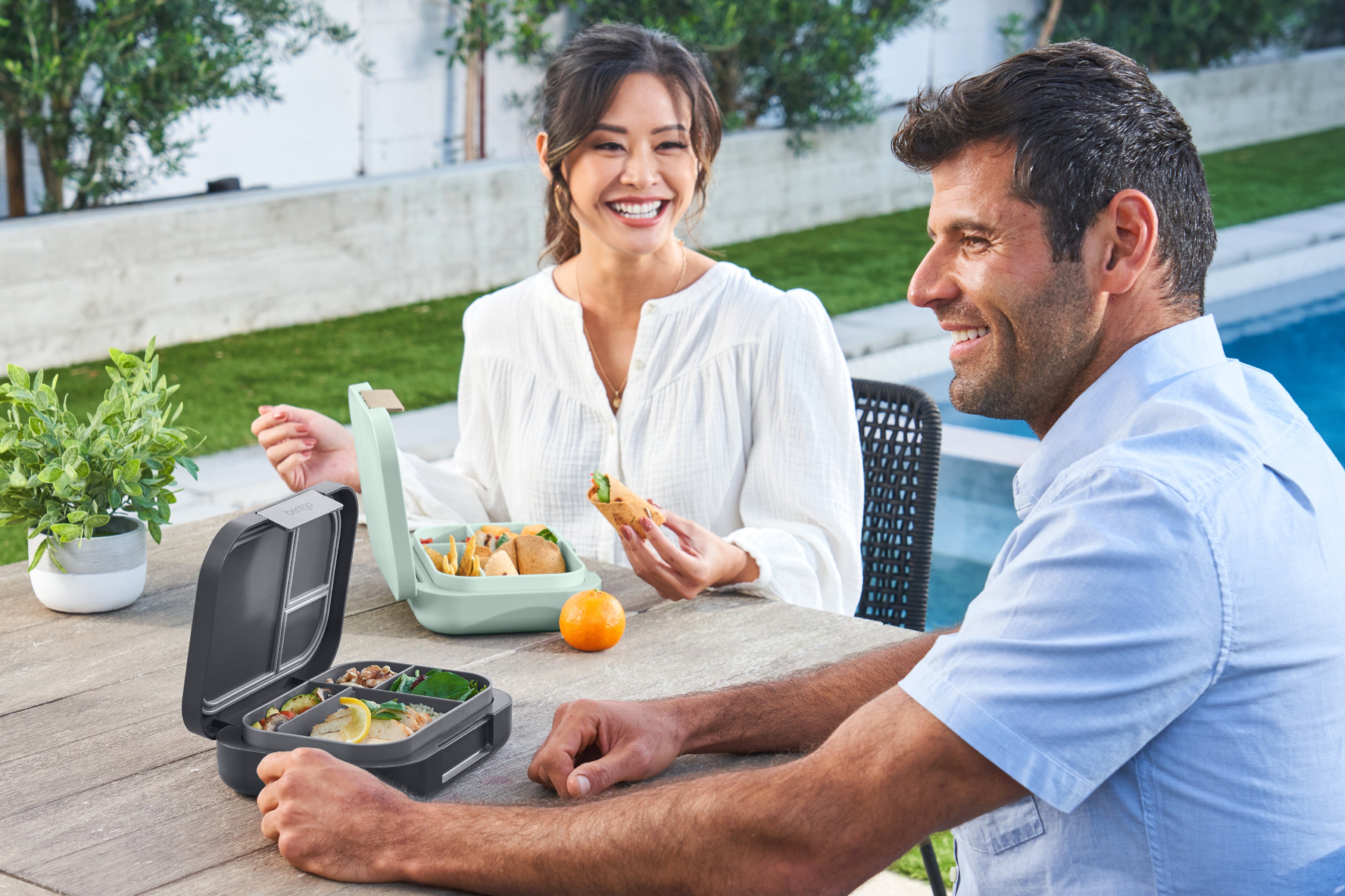 Man and woman sitting at a table outdoors with a portable food container.