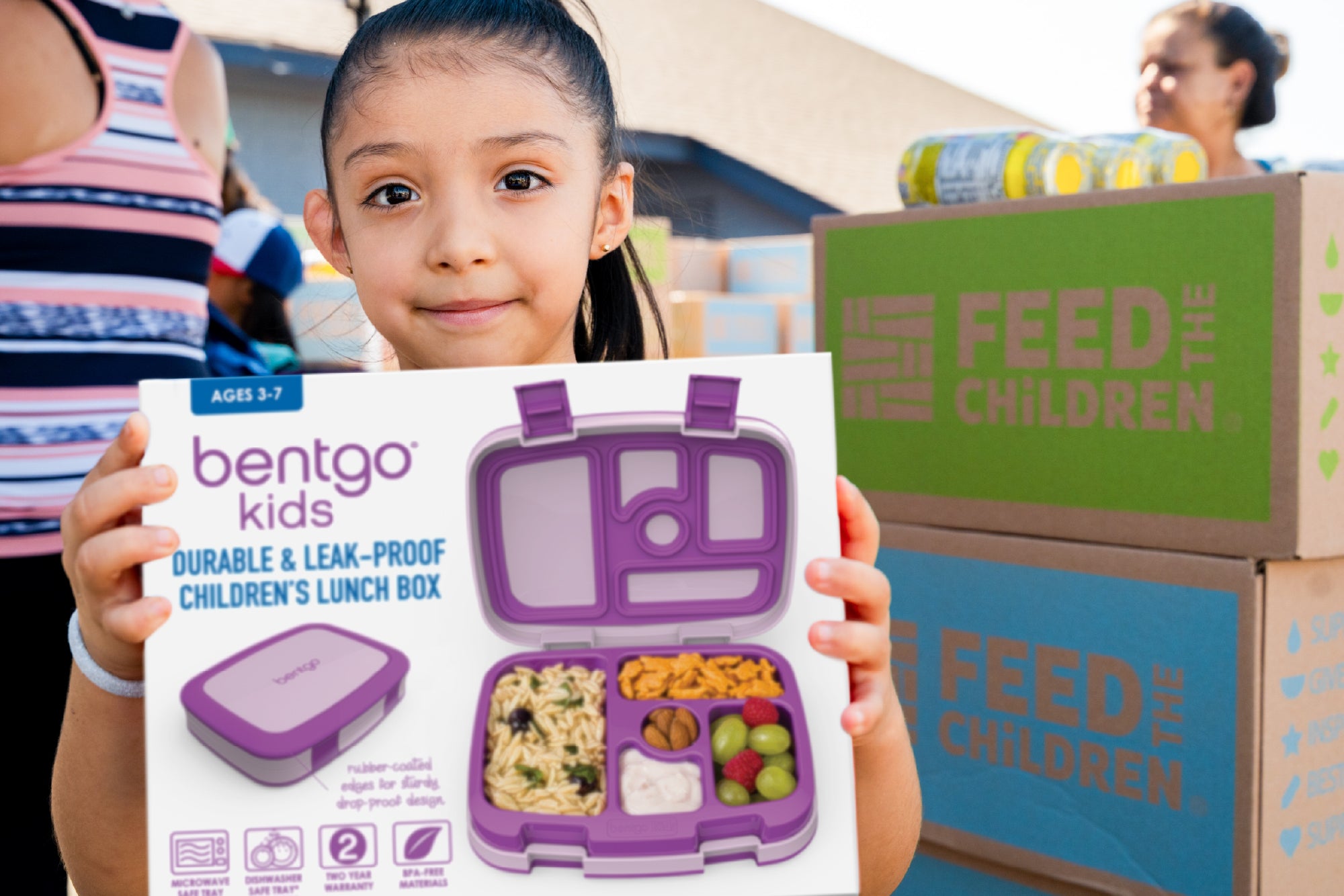 Child holding a purple bentgo kids lunch box with 'Feed the Children' boxes in the background