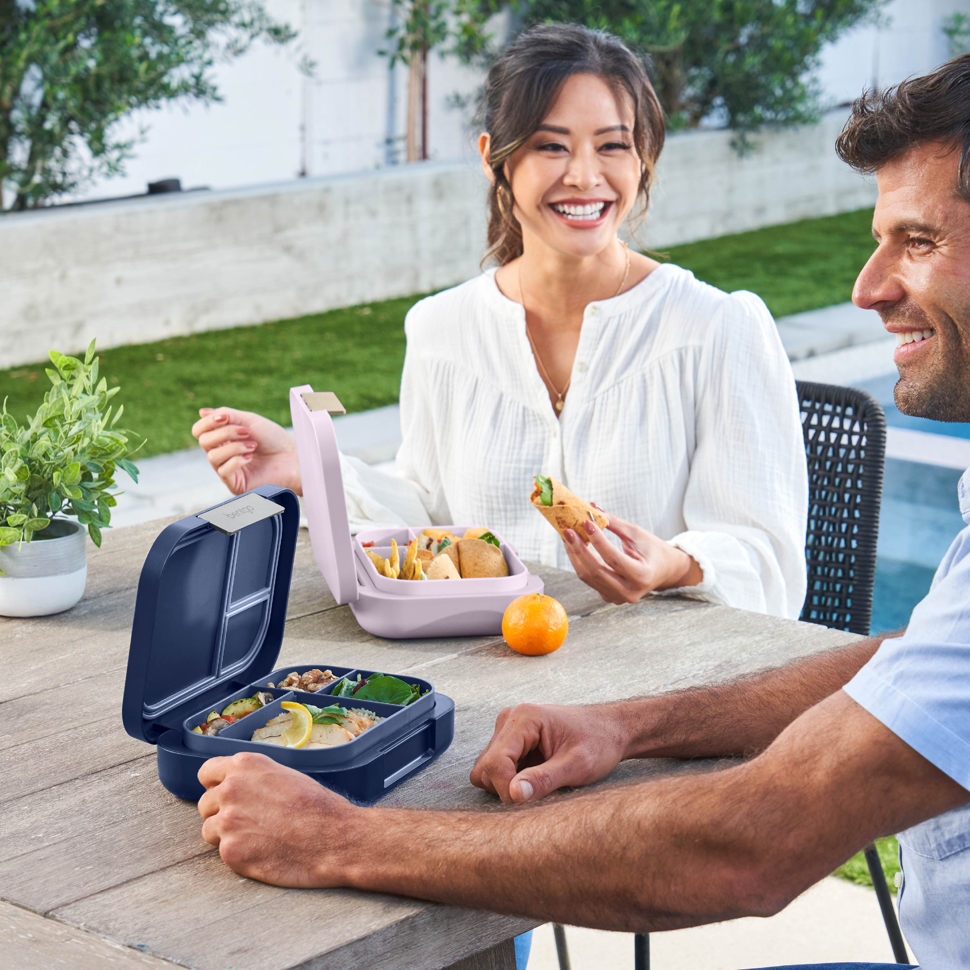 Two people enjoying a meal outdoors with bento boxes on a table.