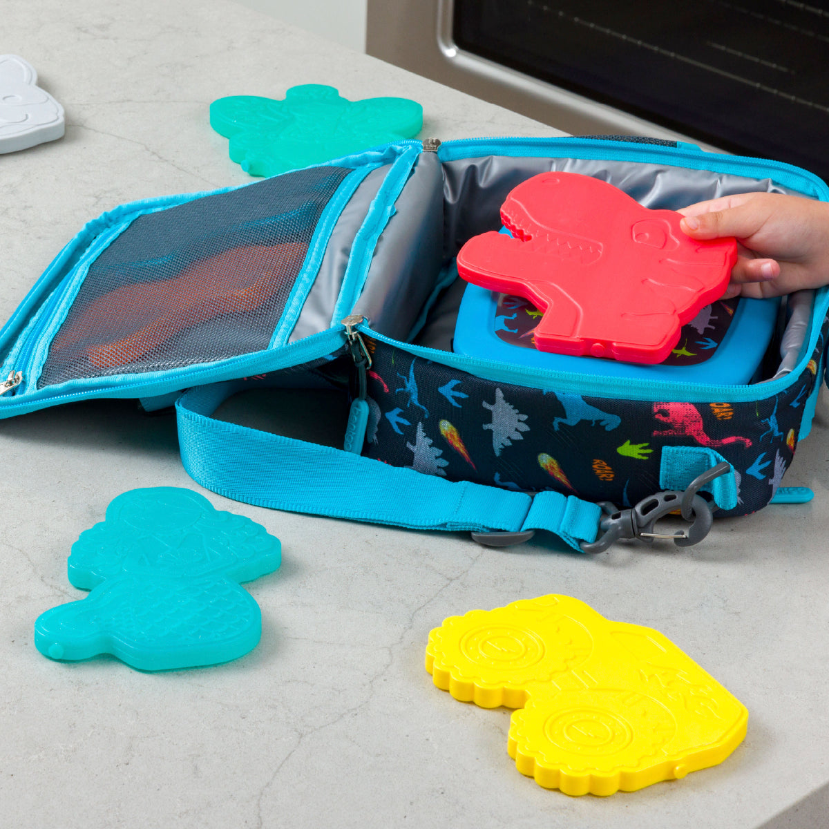 Children's lunch bag with dinosaur pattern containing colorful foam shapes on a concrete floor.