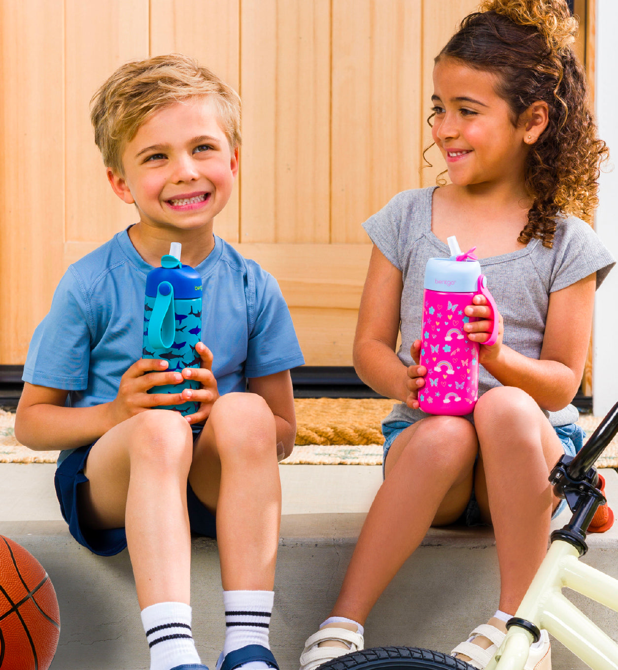 Two kids sitting outside holding water bottles